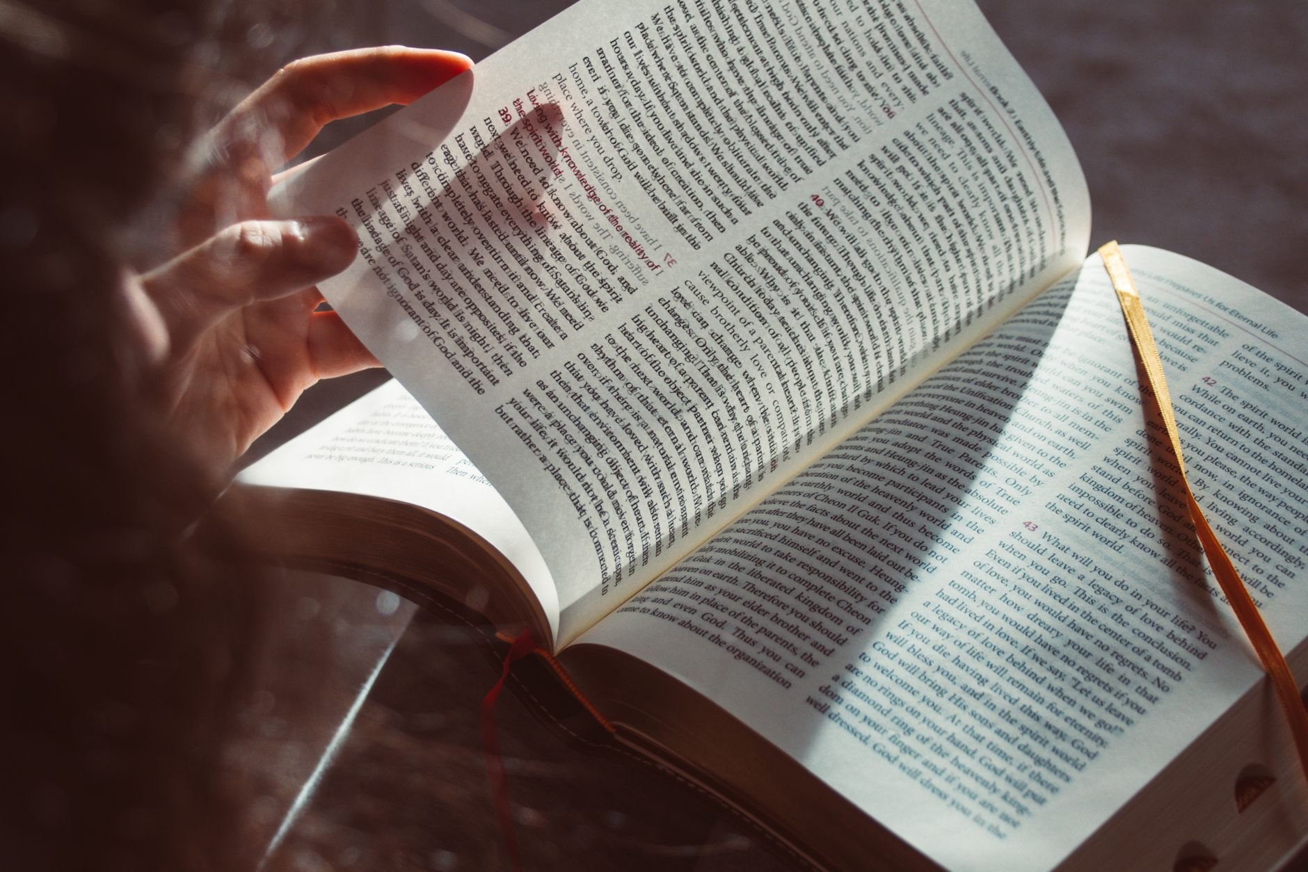 A hand gently turning a page of an open book in sunlight
